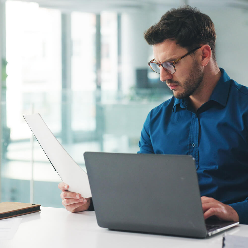 Profissional analisando relatório financeiro no notebook durante avaliação contábil para teste de impairment