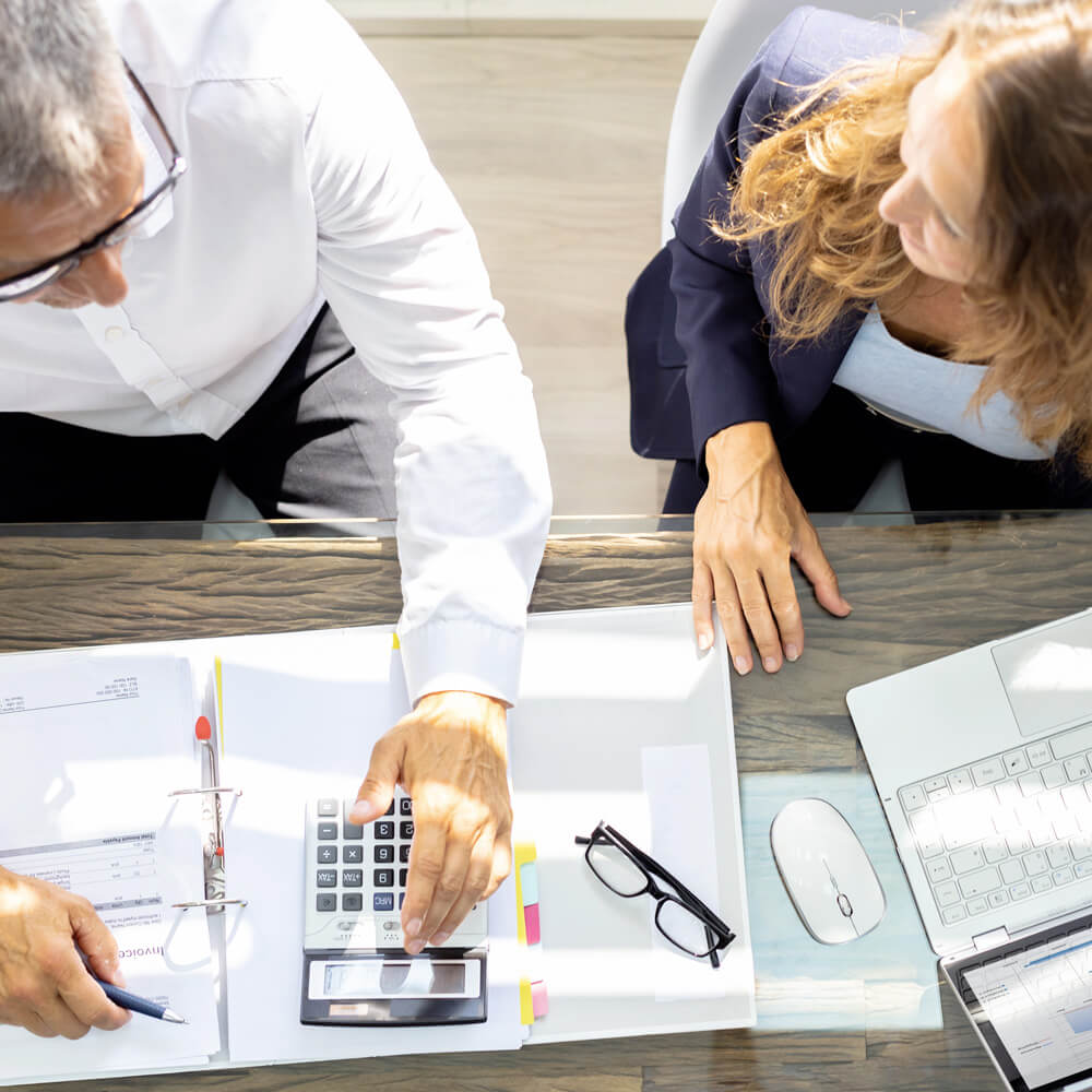 Profissionais analisando documentos e calculadora em mesa durante aplicação de metodologia de outsourcing de controle patrimonial